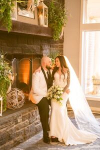 Bride and groom by the lit fireplace.