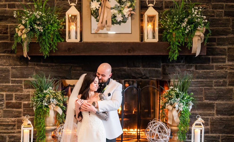 Bride and groom by the lit fireplace.