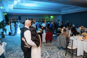 Bride and groom watch their guests dance on the dancefloor.