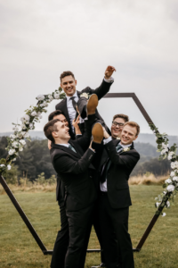 Groom being held up high by groomsmen.
