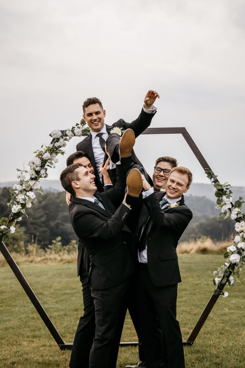 Groom being held up high by groomsmen.