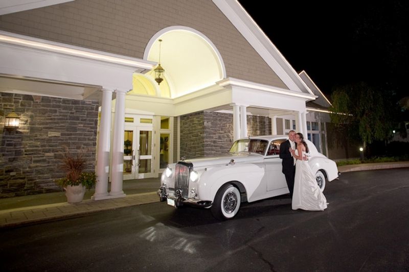 Bride and groom leaning on a classic 1950's car.