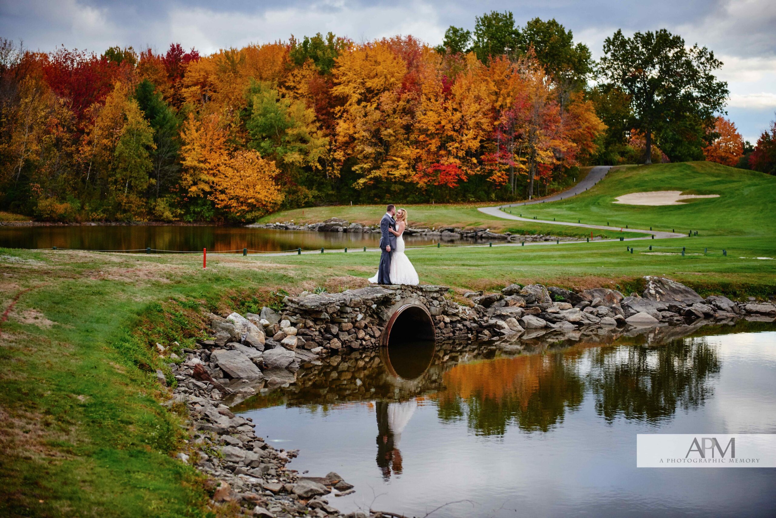 Bride and groom photo by the water in front of the fall colors of the background trees.