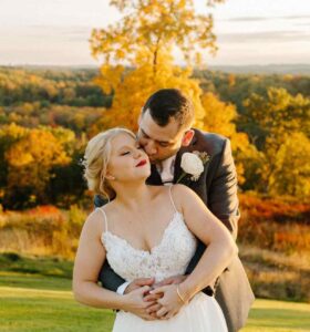 Groom kisses bride in front of the beautiful fall colors of the local foliage.