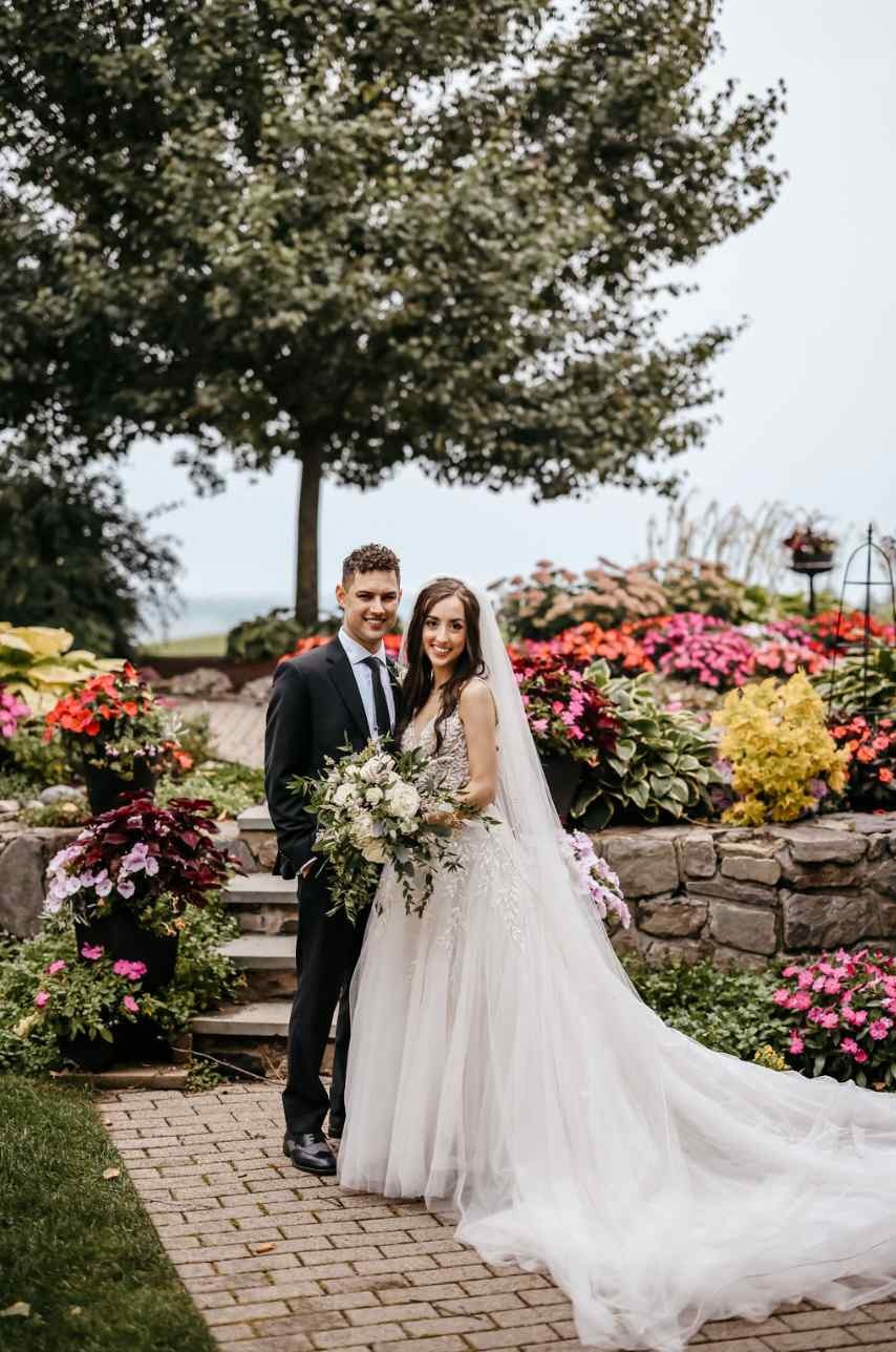 Bride with elegant white bouquet and groom take a photo in the garden.