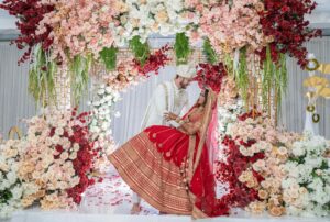 Wedding photo of a bride and groom in traditional South Asian garb in front of the flower-covered altar.