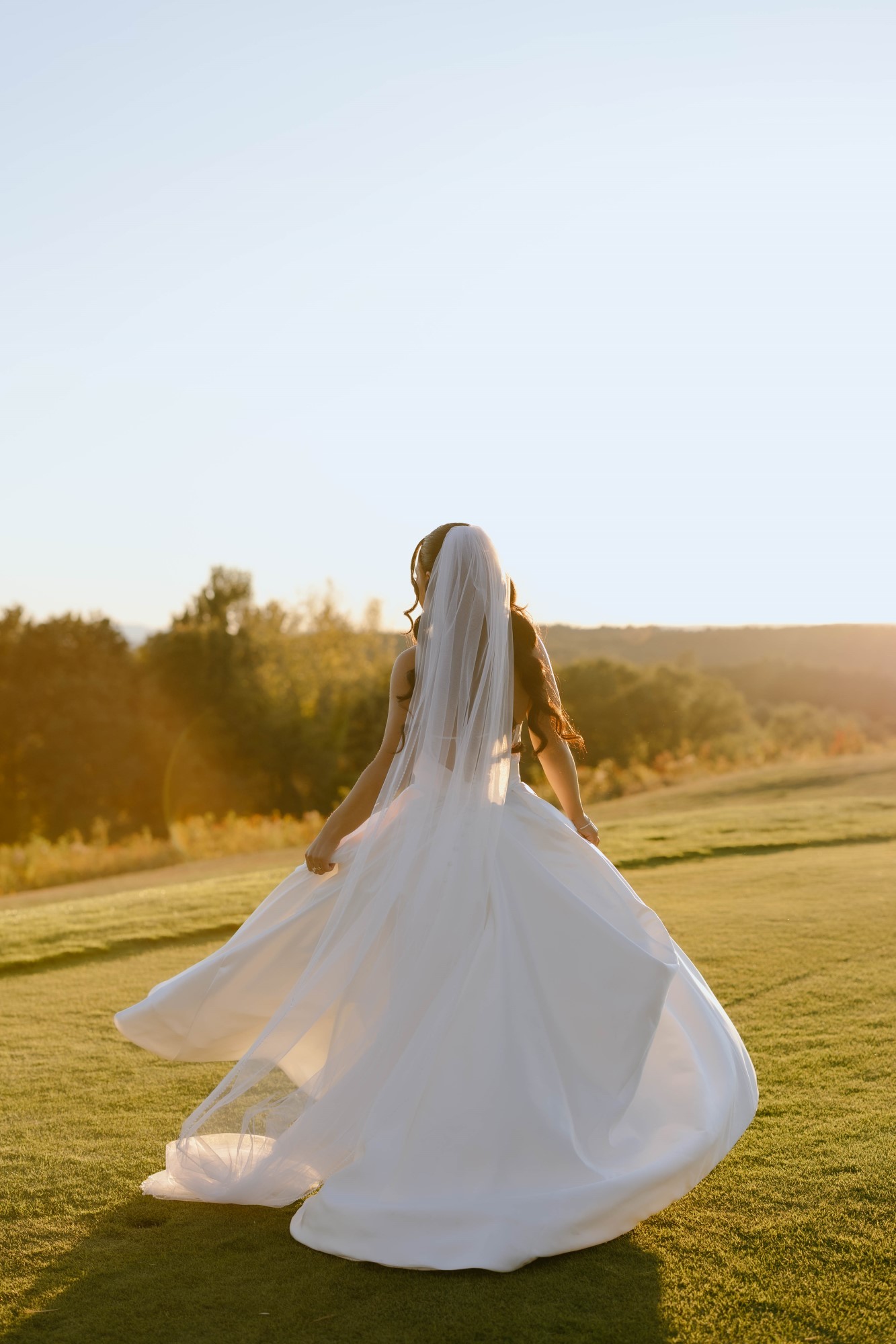 Bride stands on the grass in the sun.